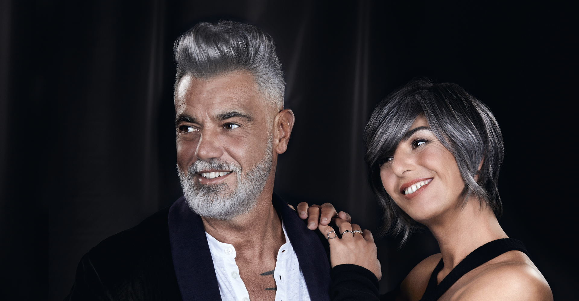 Immagine di un uomo con capelli grigi e una donna con capelli grigi appoggiata alle sue spalle. capelli corti e grigi